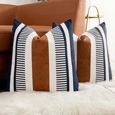 three pillows sitting on top of a white rug next to a brown couch and chair