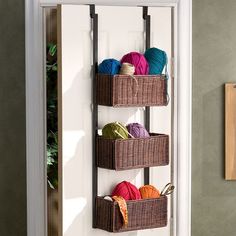 three baskets holding yarn are hanging on the wall next to an open door with a hook