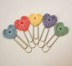 six crocheted heart shaped paper clips on a white surface with pins in the shape of hearts