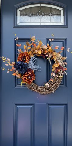 a blue front door with a wreath on it and autumn leaves hanging from the side