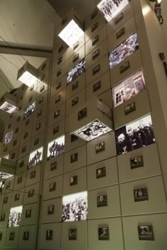 a wall with many pictures on it and lights above the photo is hanging from the ceiling