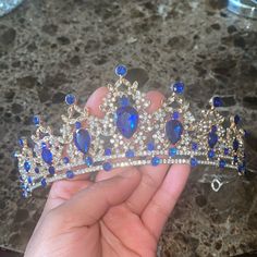 a hand is holding a tiara with blue and white stones on it's sides