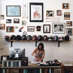 a woman sitting at a desk in front of a wall covered with pictures and helmets