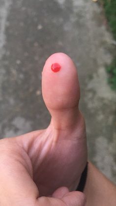 a hand holding a tiny red object in it's palm, with the thumb pointing up