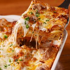 a white casserole dish filled with meat and sauce on a wooden table next to a red checkered napkin