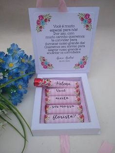 an open box with three pink candles in it next to some blue flowers and ribbon