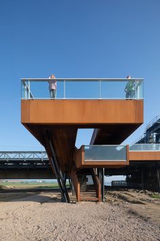 two people standing on top of a wooden structure over looking the water and beach below