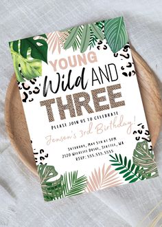 the wild and three birthday party is set on top of a wooden plate with greenery