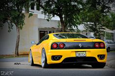 the rear end of a yellow sports car parked in front of a tree and building