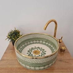 a green and white bowl sitting on top of a wooden table next to a potted plant