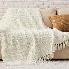 a couch with a blanket on top of it next to pillows and a brick wall