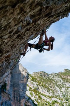 a woman climbing up the side of a cliff with her hands in the air while holding onto a rope