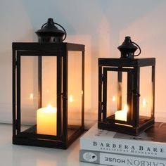 two lit candles sitting next to each other on top of a white table with books