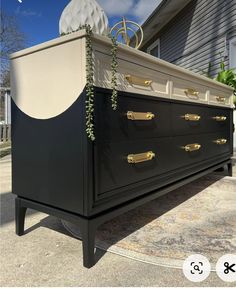 an old dresser is painted black and white with gold hardware on the bottom, along with a plant growing out of it