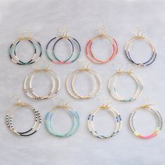 six pairs of hoop earrings in various colors and sizes on a white surface with gold earwires