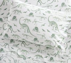 an image of dinosaur bedding set with green dinosaurs on white sheets and pillow cases