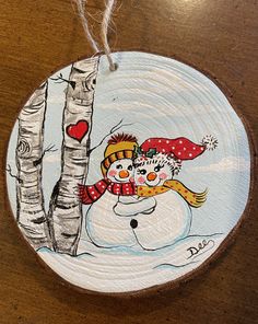 a wooden ornament with a snowman and a birch tree painted on it