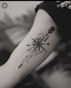 a woman's arm with an arrow and compass tattoo on the left side of her arm