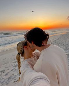 a man and woman kissing on the beach at sunset