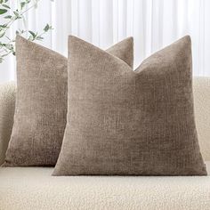 two brown pillows sitting on top of a couch next to a potted green plant