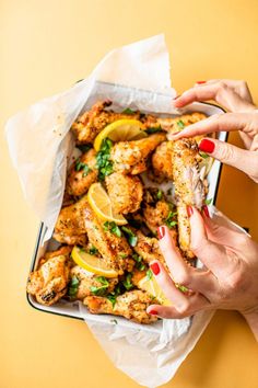 two hands holding a sandwich with chicken wings and lemon wedges