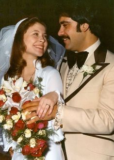 a bride and groom pose for a photo together in their wedding day attire, with flowers on the bouquet