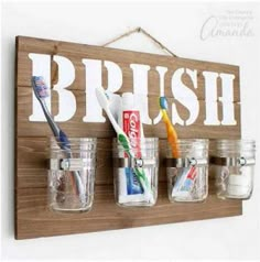 three mason jars with toothbrushes and toothpaste in them hanging on a wall