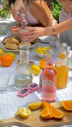 two women at a table with oranges, lemons and bottles of alcohol on it