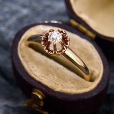 a gold ring with a diamond sits in a wooden box on top of a cloth covered surface