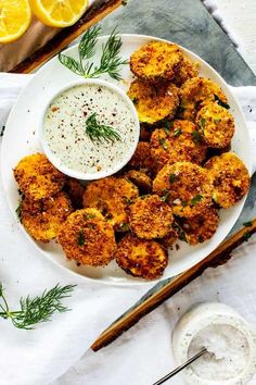 a white plate topped with tater tots next to a bowl of ranch dressing