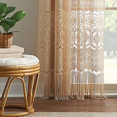 a plant in a basket on top of a stool next to a window with sheer curtains