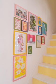 there are many framed pictures on the wall next to the stair case in this house