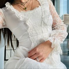 a woman wearing a white dress and holding her hand on her hip while sitting in front of a window