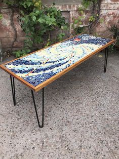 a table made out of mosaic tiles and hairpink legs on the ground in front of a brick wall