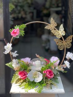 an arrangement of flowers and butterflies in a metal ring on a table outside the store