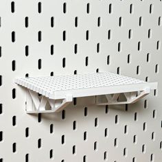 a white shelf mounted to the side of a perfored wall with holes in it