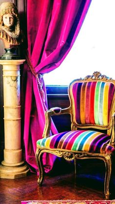 a chair sitting in front of a window next to a red drapes covered curtain