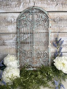 white flowers and greenery sit in front of an old metal door on a wooden wall