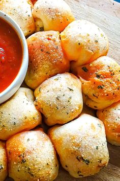 rolls with dipping sauce on top of them sitting on a cutting board next to a bowl