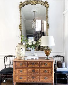 a room with a dresser, mirror and lamp on the side table in front of it