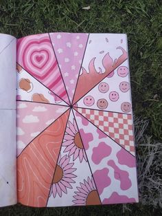 an open book sitting on top of a grass covered field next to a pink umbrella