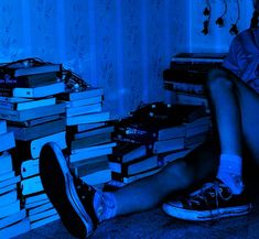 a person sitting on the floor with stacks of books in front of them and a blue light behind them