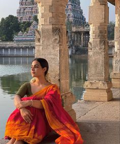 a woman in an orange and red sari sitting on the ground next to water