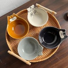 three bowls with cat faces on them are sitting in a bamboo basket next to chopsticks