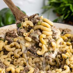 a ladle full of macaroni and cheese being held by a wooden spoon