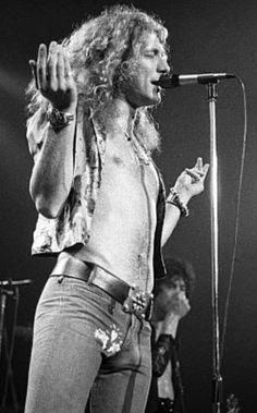 a man with long hair standing in front of a microphone and holding his hands up