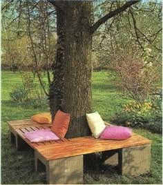 a wooden bench sitting under a tree with pillows on it's backrests