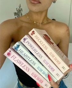 a woman holding four books in her hands and wearing red nail polish on her nails