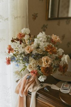 a bouquet of flowers sitting on top of a wooden dresser next to a white curtain