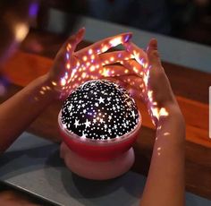 two hands reaching for a glowing object in a bowl on top of a wooden table